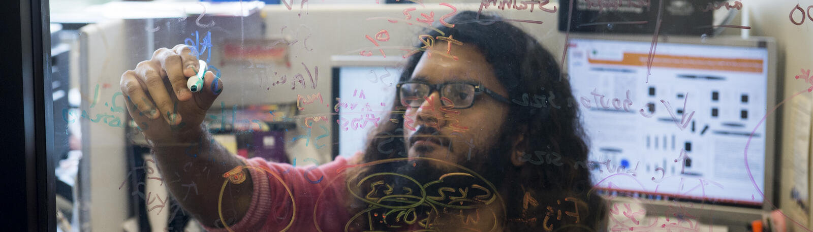 photo of a student writing on a glass window in a lab